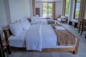 A hotel room with a large bed, multiple pillows, a bedside table, a chair, and a view of greenery outside. - Stone Age Boutique  (Kampot)