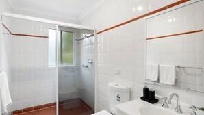 A modern bathroom with white tiles, a glass shower enclosure, a white toilet, a sink with a mirror, and a towel rack. - Gorgeous Griffith 2Bed/1Bath Pad (Griffith)