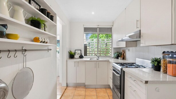 A modern kitchen with white cabinets, a gas stove, and a window with a view of greenery. - Gorgeous Griffith 2Bed/1Bath Pad (Griffith)