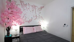 Un dormitorio con cama, mesita de noche, lámpara y pared decorada con motivos de cerezos.