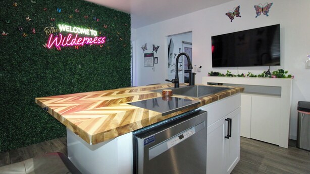 Una cocina moderna con encimera de madera en espiga, lavavajillas y un letrero de neón en la pared.