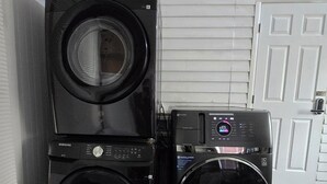 Una lavadora y secadora apiladas en un cuarto de lavado, con una puerta blanca al fondo.