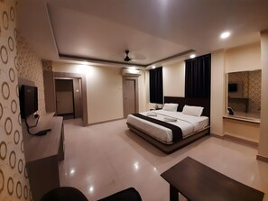 A modern hotel room with a large bed, a desk, a flat-screen TV, and a ceiling fan. - THE OCEAN (Brahmagiri)