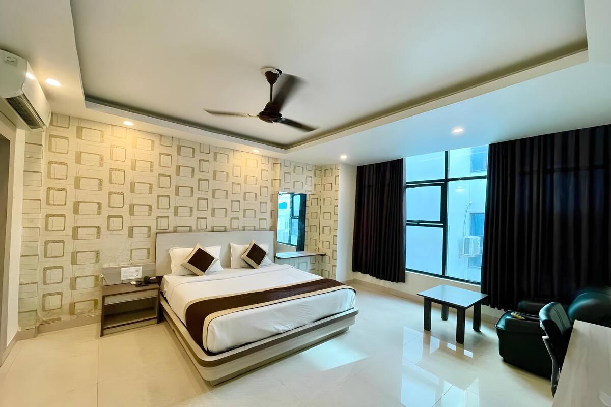 Une chambre d’hôtel moderne avec un grand lit, un ventilateur de plafond, une petite table et une vue sur l’extérieur par une fenêtre.
