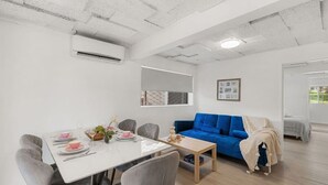Ein modernes Wohnzimmer mit Essbereich, ausgestattet mit einem blauen Sofa, grauen Sesseln und einem weißen Esstisch, der gedeckt ist.