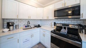 A modern kitchen with white cabinets, a stainless steel microwave, and a built-in oven. - OV Mosaic - Coconut Suite (Norfolk)