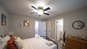 Un dormitori amb un llit, un ventilador de sostre, un armari i una porta que dona a una altra habitació.