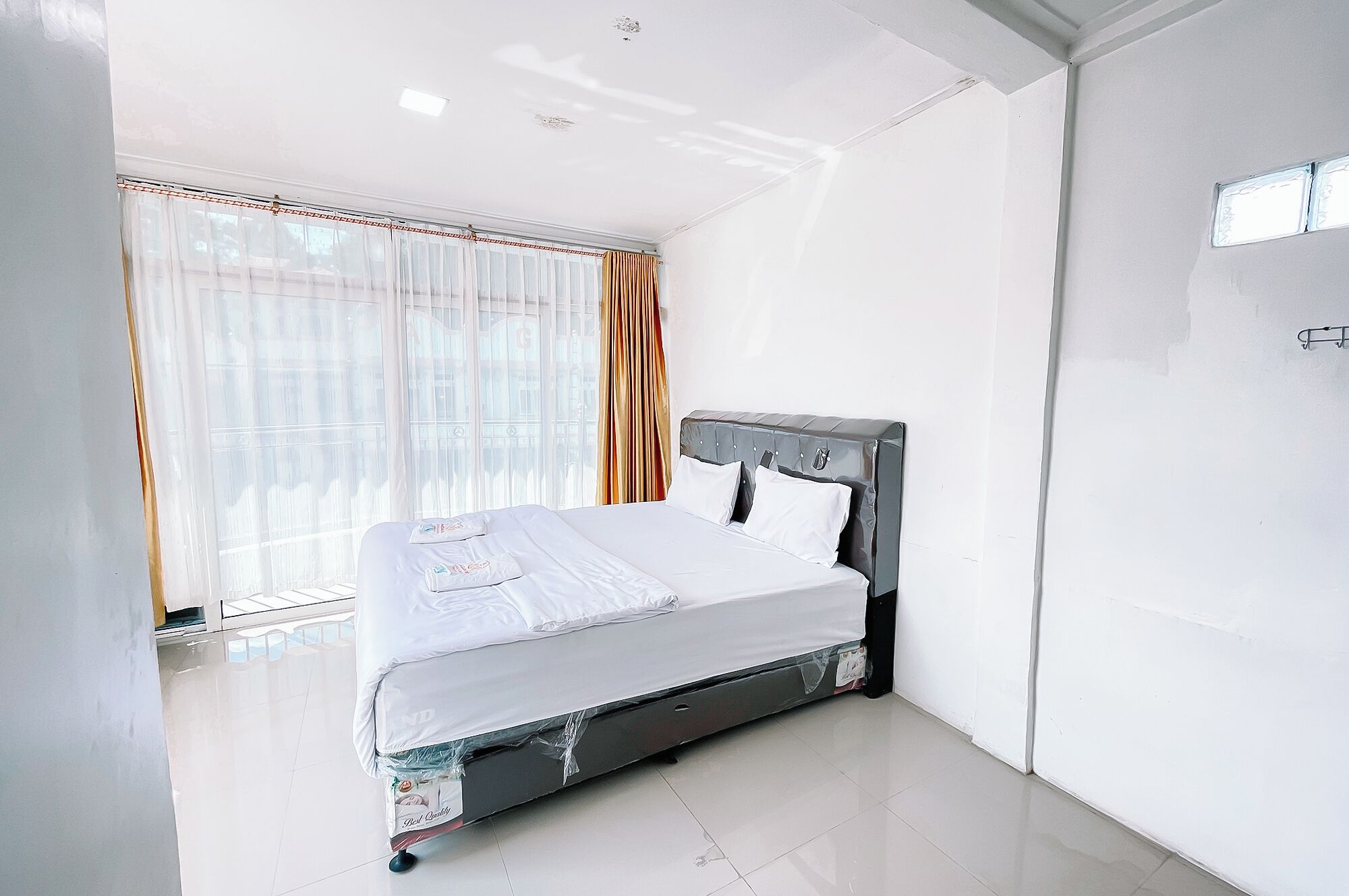 A modern bedroom with a bed, a window with sheer curtains, and a view of the city.