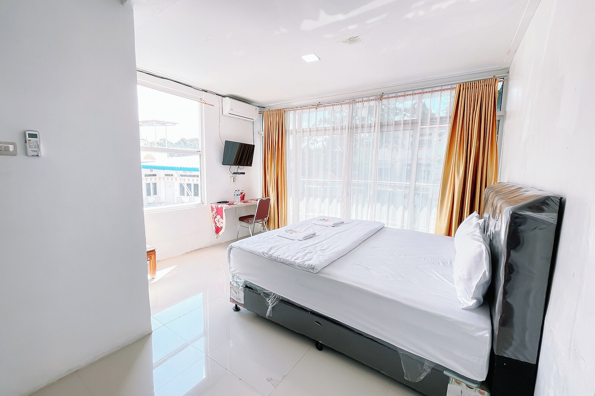 A hotel room with a bed, a desk, a chair, a TV, and a window with curtains.