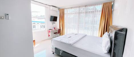 A hotel room with a bed, a desk, a chair, a TV, and a window with curtains.
