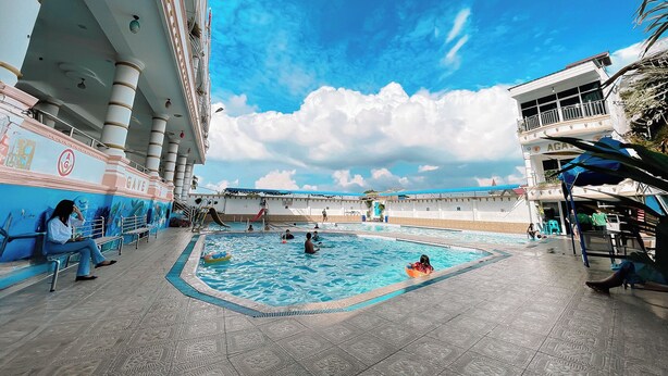 A pool area with a large pool, a slide, and a seating area with people. - Agave Hotel By Helocus (Pematang Pane)