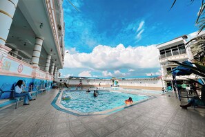Un área de piscina con una pileta grande, un tobogán y una zona de estar con gente.