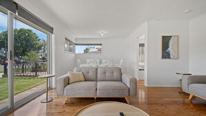 Una sala de estar moderna con un sofá gris, una mesa de centro redonda y vistas al exterior a través de amplios ventanales.