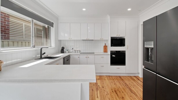 Una cocina moderna con armarios blancos, un refrigerador negro y piso de madera.