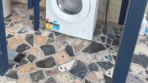 Une machine à laver à chargement frontal, située dans un espace buanderie avec un sol carrelé et un mur en briques.
