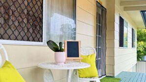 A covered porch with white metal chairs, a small round table, and a potted plant.