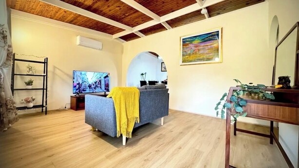 A living room with a grey sofa, wooden ceiling beams, a TV, and a painting on the wall.
