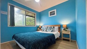 A bedroom with a bed, a nightstand, a window with a view, and a ceiling fan.