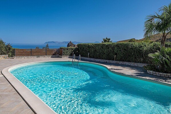 Una piscina con vistas claras al océano y montañas al fondo.