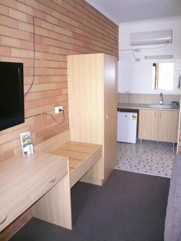 A compact room with a wooden desk, a small kitchenette, and a TV mounted on the wall. - Grong Grong Motor Inn (Grong Grong)