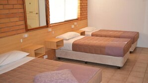Ένα δωμάτιο ξενοδοχείου με τρία κρεβάτια, το καθένα με ξύλινο π ροσκέφαλο, λευκά σεντόνια και ένα μικρό κομοδίνο.