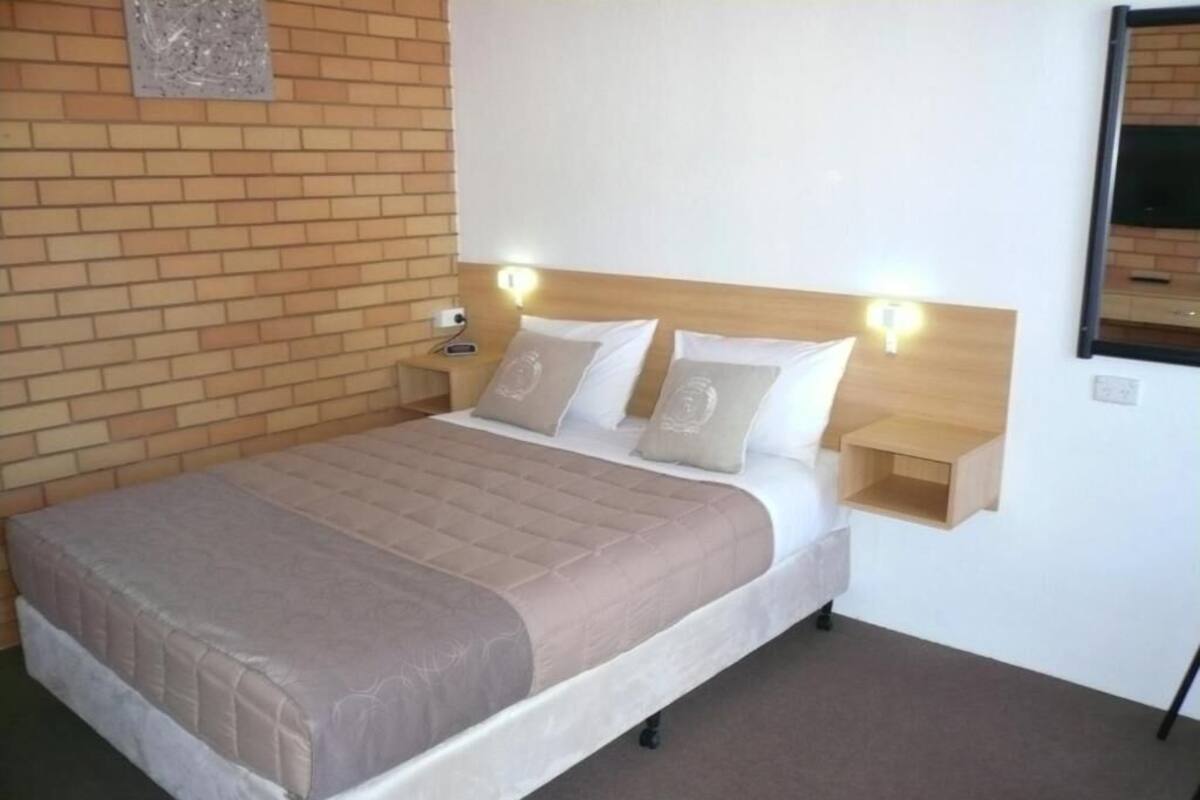 A neatly made bed with a headboard, a bedside table, and a wall-mounted light fixture.