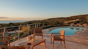 A poolside area with a view of the sea, outdoor seating, and a stone pathway.