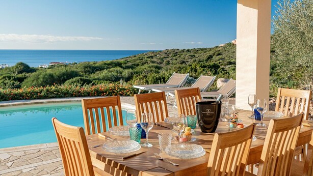 A dining table set for six with a view of the sea and hills.