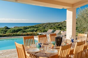 Mesa de comedor lista para seis personas, con vista al mar y las colinas.
