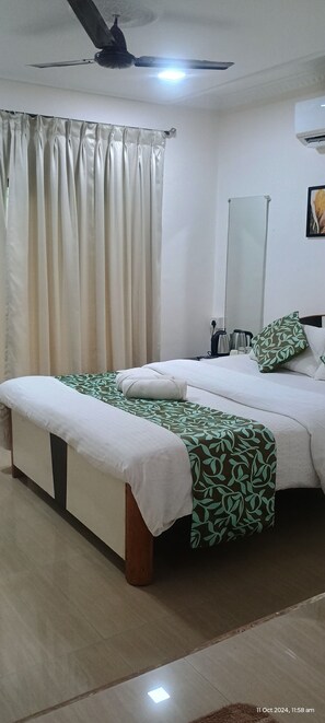 A hotel room with a bed, a bench, a ceiling fan, a mirror, and a window with curtains. - Riverstone Nature Resort (Dapoli)