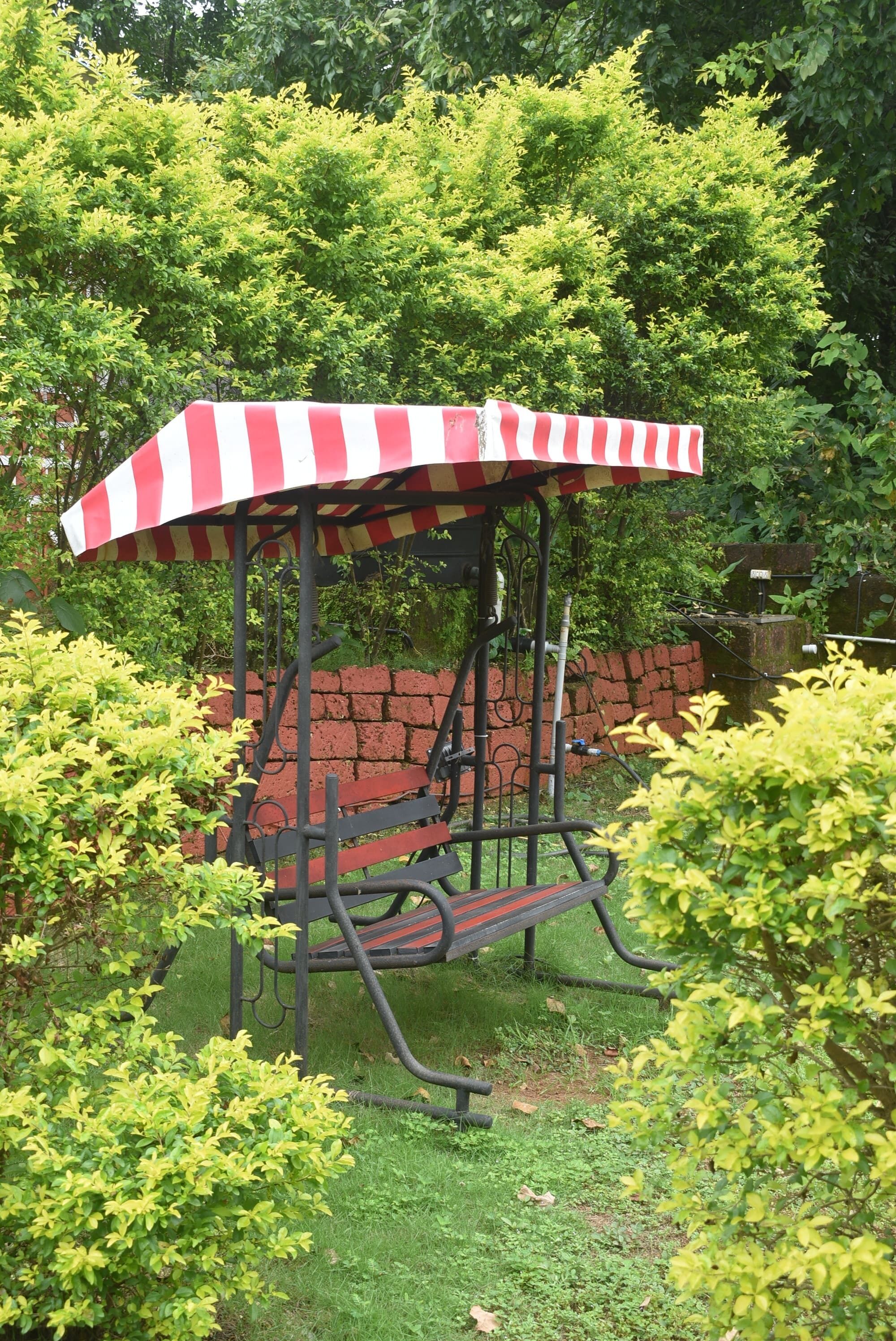 A garden gazebo with a striped canopy, surrounded by lush greenery and a brick wall.