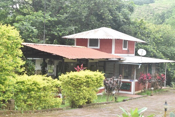 A red building with a tiled roof, surrounded by lush greenery and a satellite dish. - Riverstone Nature Resort (Dapoli)