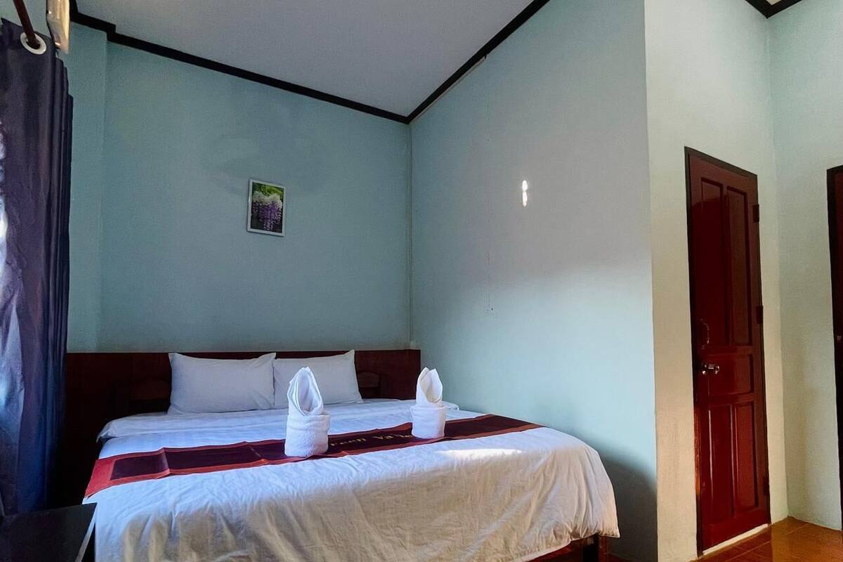 A hotel room with a bed, a ceiling fan, a door, and a wall with a small picture.
