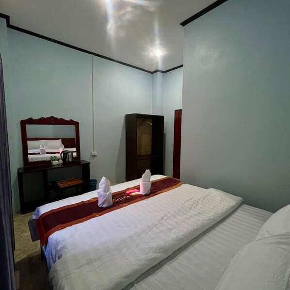 Une chambre d’hôtel avec un lit bien fait, une commode en bois, un miroir et une armoire.