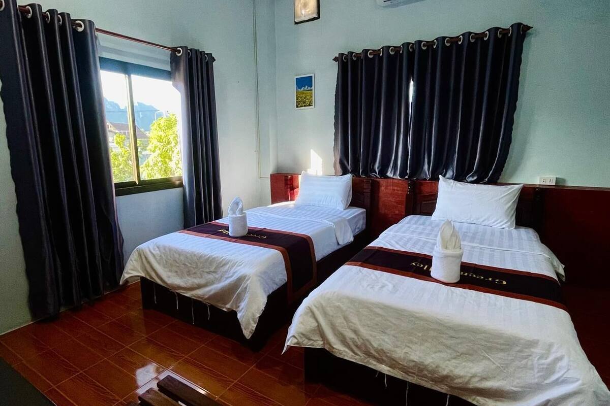A hotel room with two beds, a wooden table, and a window with curtains.