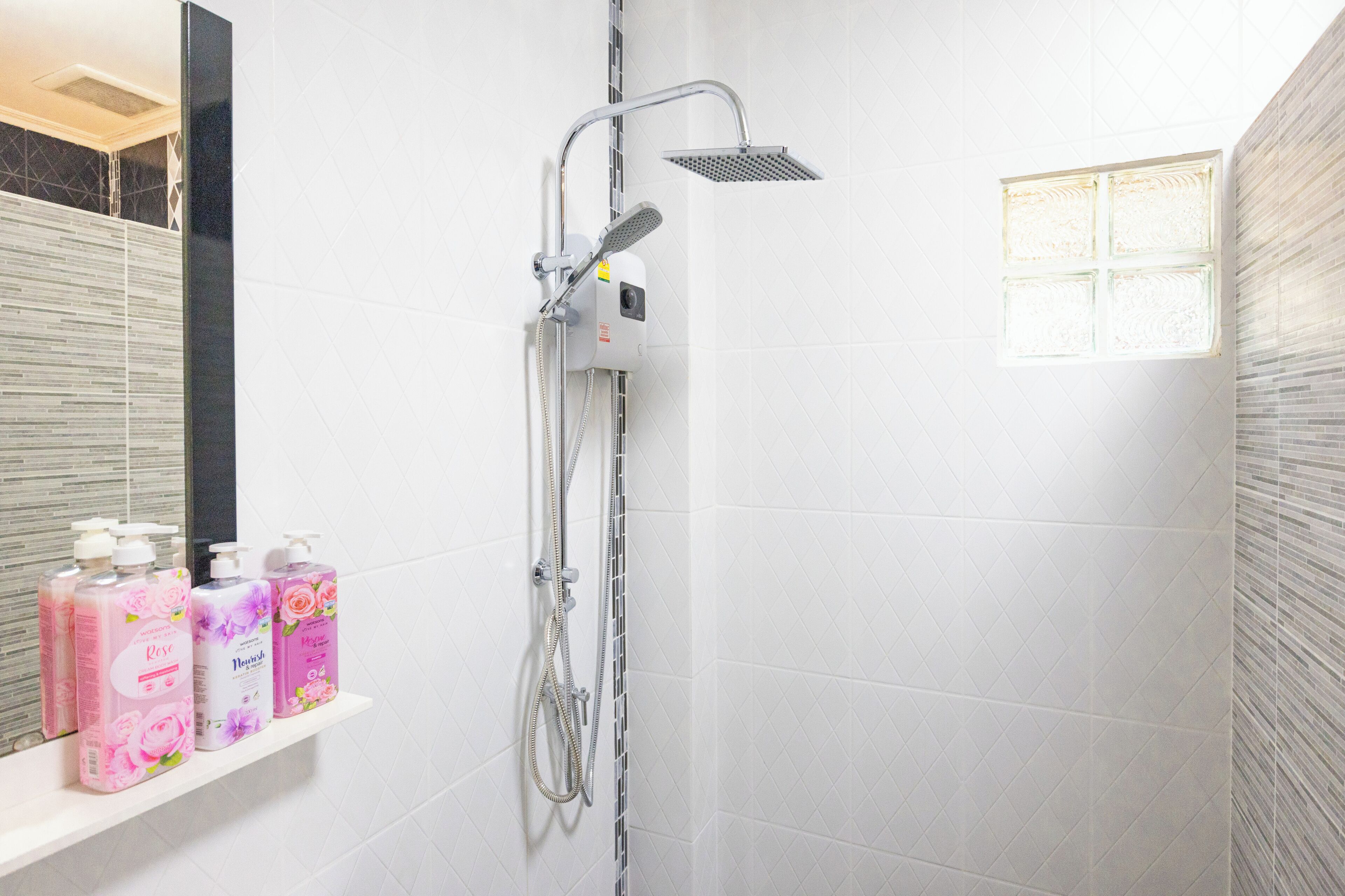 Un baño con ducha, espejo y repisa con tres botellas de jabón líquido.