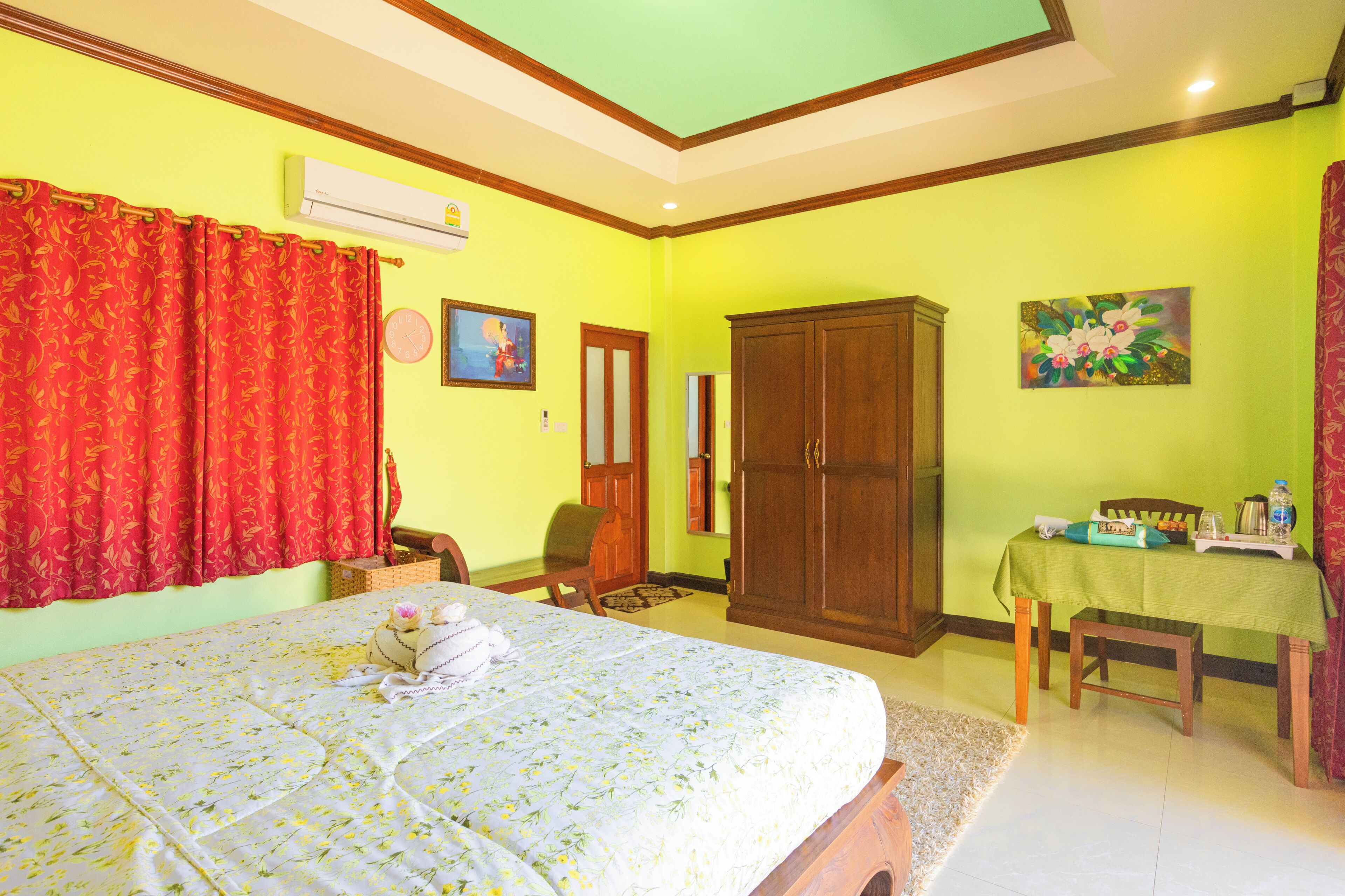 A bedroom with a bed, a wooden wardrobe, a dining table with a green tablecloth, and a red curtain.