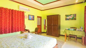 A bedroom with a bed, a wooden wardrobe, a dining table with a green tablecloth, and a red curtain.