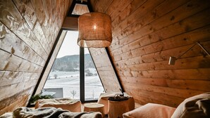 A cozy room with wooden walls, a sloped ceiling, and a large window offering a view of a snowy landscape.