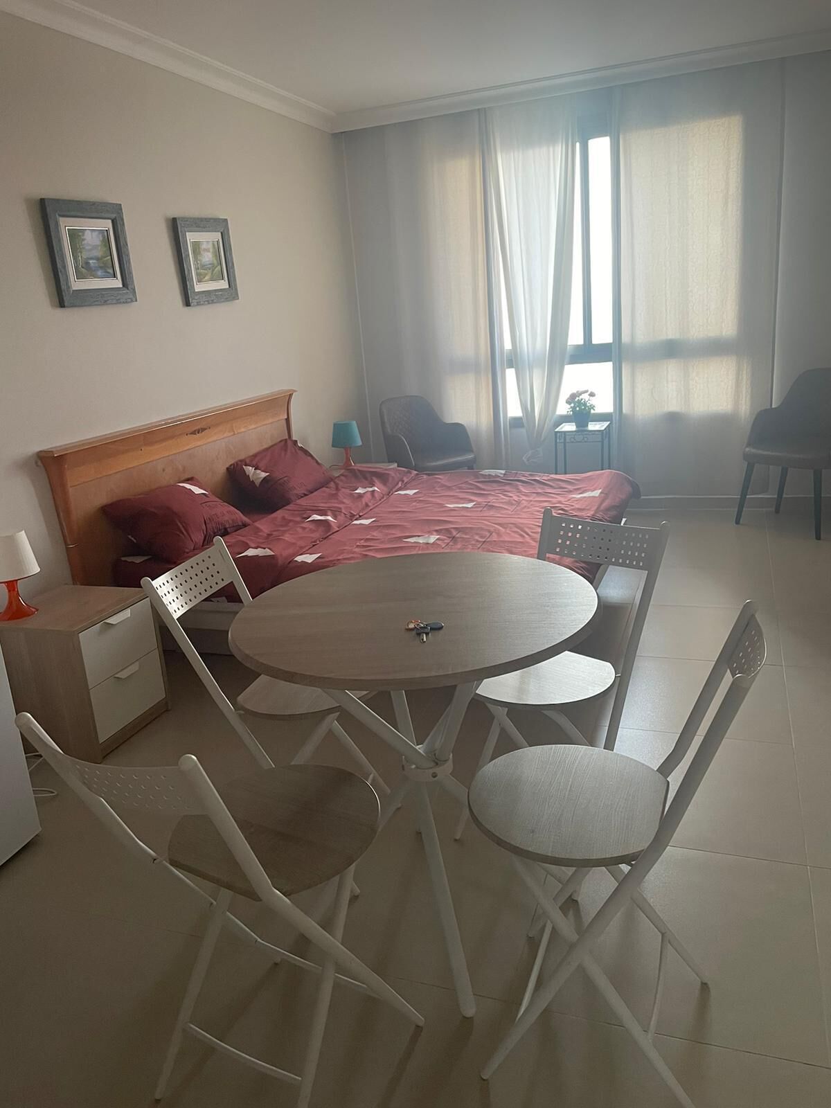 Una habitación de hotel con cama, una mesa redonda con sillas, un escritorio pequeño y un ventanal con cortinas.