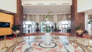Un amplio vestíbulo con una fuente decorativa central, ventanas grandes y plantas en macetas.