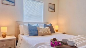 Een keurig opgemaakt bed met een dienblad vol roze bloemen, twee kopjes en een schaal koekjes.