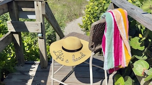Een houten terras met uitzicht op het strand, een strohoed en een kleurrijke handdoek.