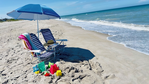 Een strand met twee gestreepte ligstoelen en een blauwe parasol.