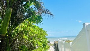 Een pad dat naar een strand leidt, met een wit hek en weelderige begroeiing.
