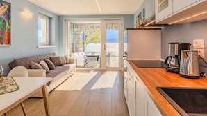 Une cuisine moderne avec un plan de travail en bois, une machine à café et une vue sur la mer, visible à travers la porte-fenêtre coulissante.