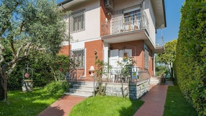 Une maison à deux étages dotée d’un balcon, d’un escalier en pierre et d’un jardin bien entretenu.