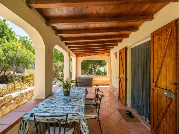 Un porche cubierto con una mesa y sillas, una planta en maceta y vistas del jardín.