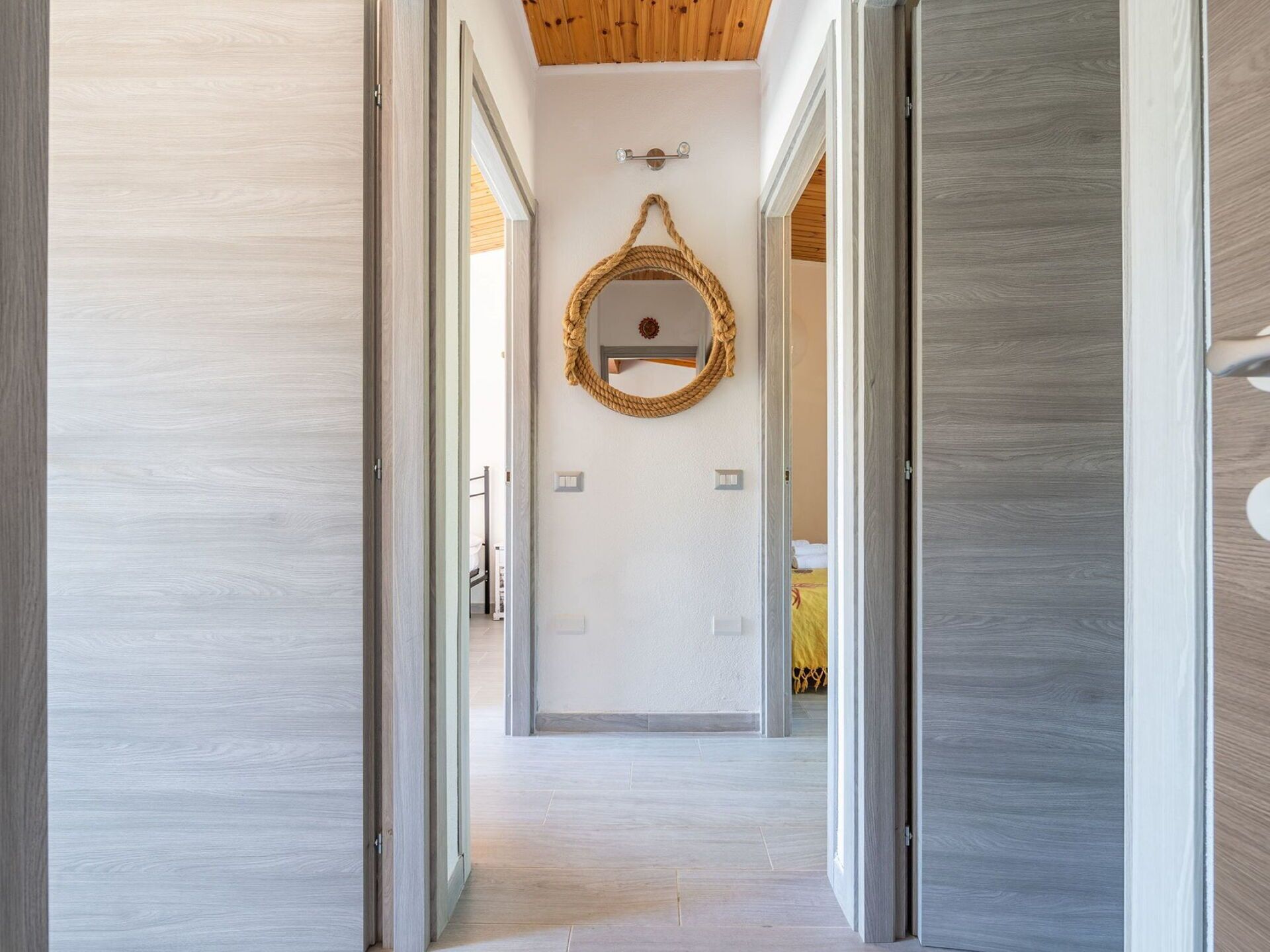 Un pasillo con pisos de madera, un espejo en la pared y puertas que dan a otras habitaciones.