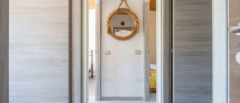 Un pasillo con pisos de madera, un espejo en la pared y puertas que dan a otras habitaciones.